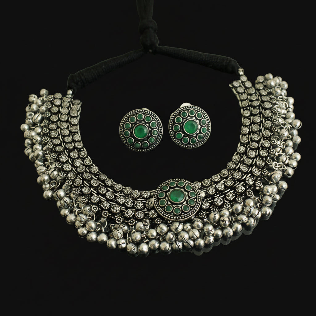 Silver necklace with green gemstones and matching earrings on a dark background