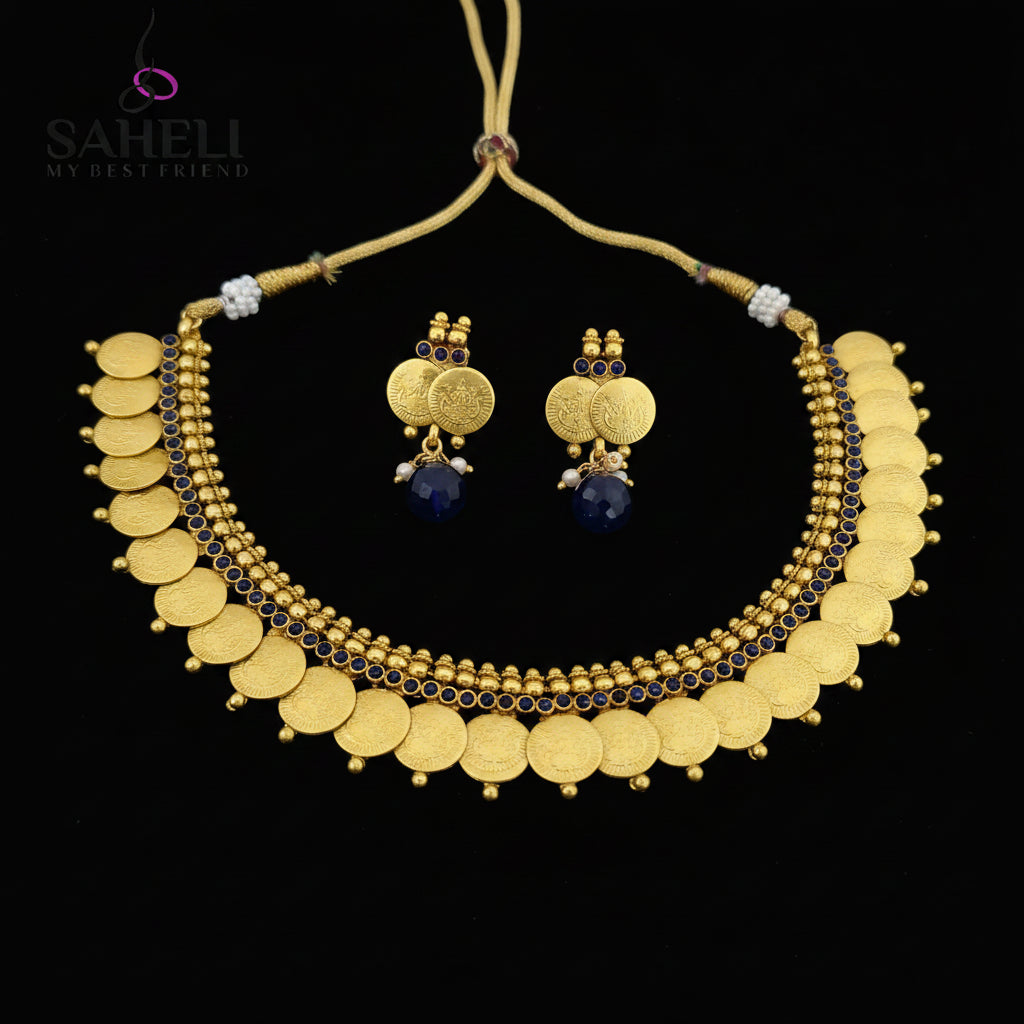 Gold coin necklace and matching drop earrings displayed on a dark reflective surface. The necklace features multiple rows of gold coins, small gold beads, and dark blue stone accents, with a gold cord closure.