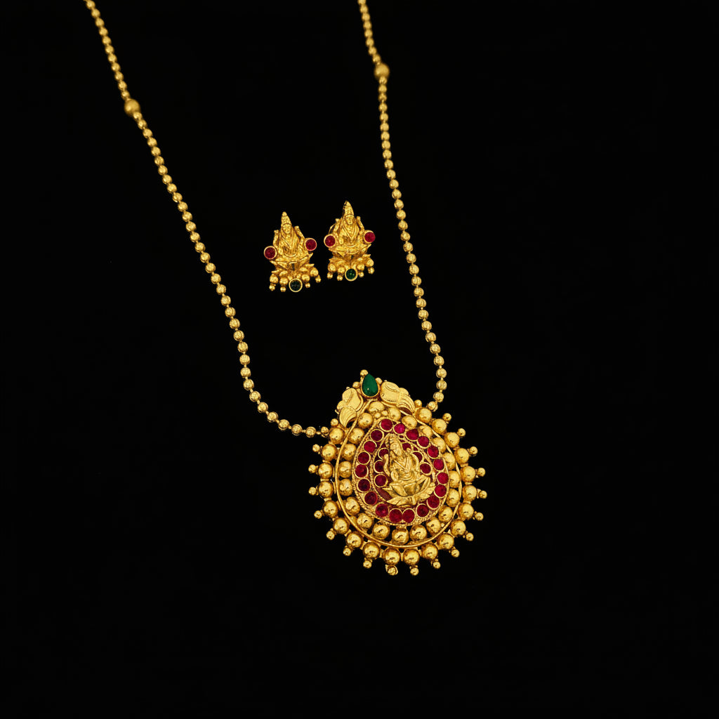 Gold-toned traditional necklace and matching stud earrings with red and green stone accents, displayed on a dark gray reflective surface. The SAHeli My Best Friend logo appears in the upper left corner.