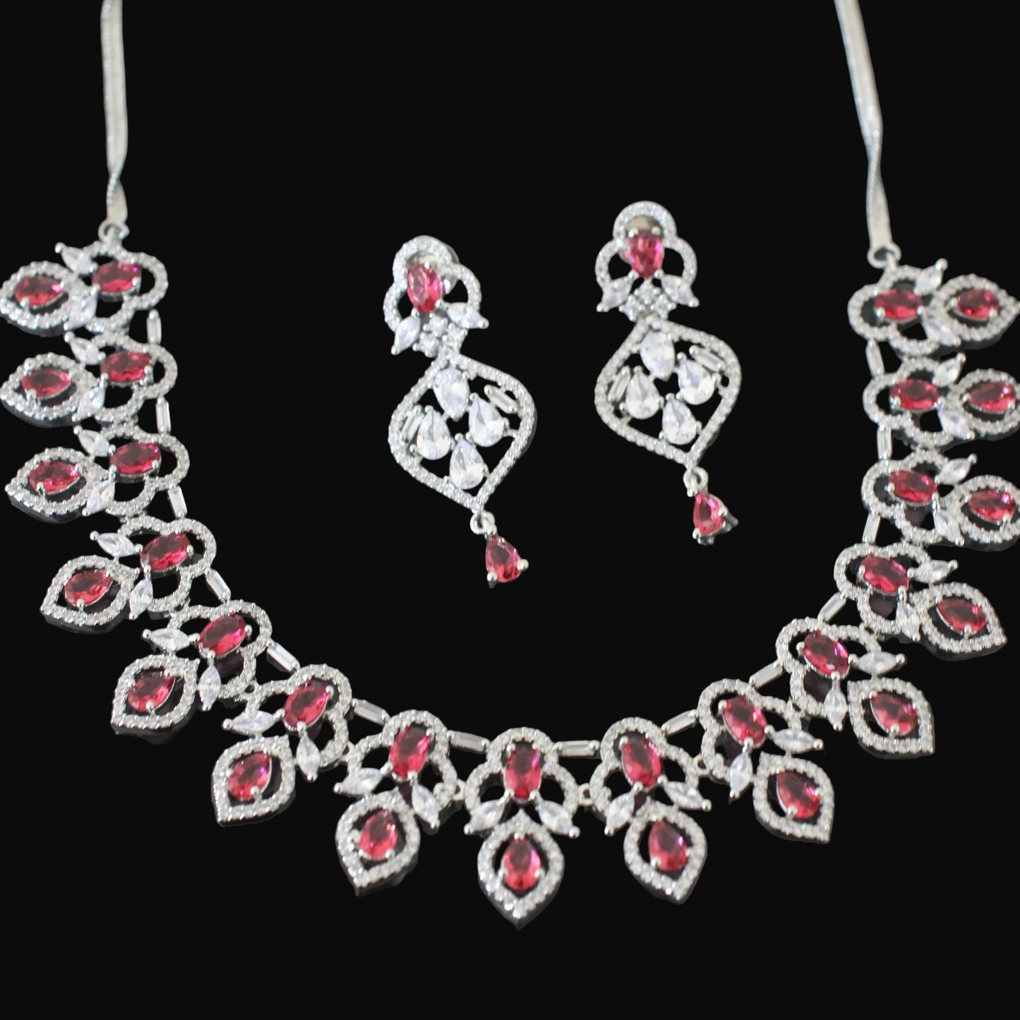 Jewelry set with necklace and earrings featuring red stones on a dark background, branded 'Saheli'.