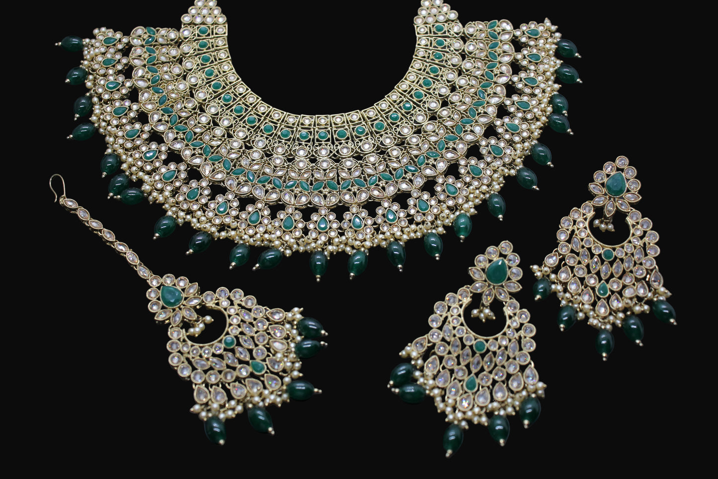Ornate necklace and earrings set with green stones on a dark background