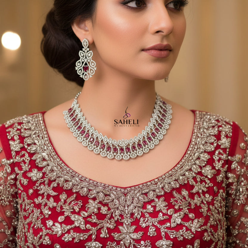 Silver necklace with red stones and matching earrings on a dark background, branded 'Saheili'.