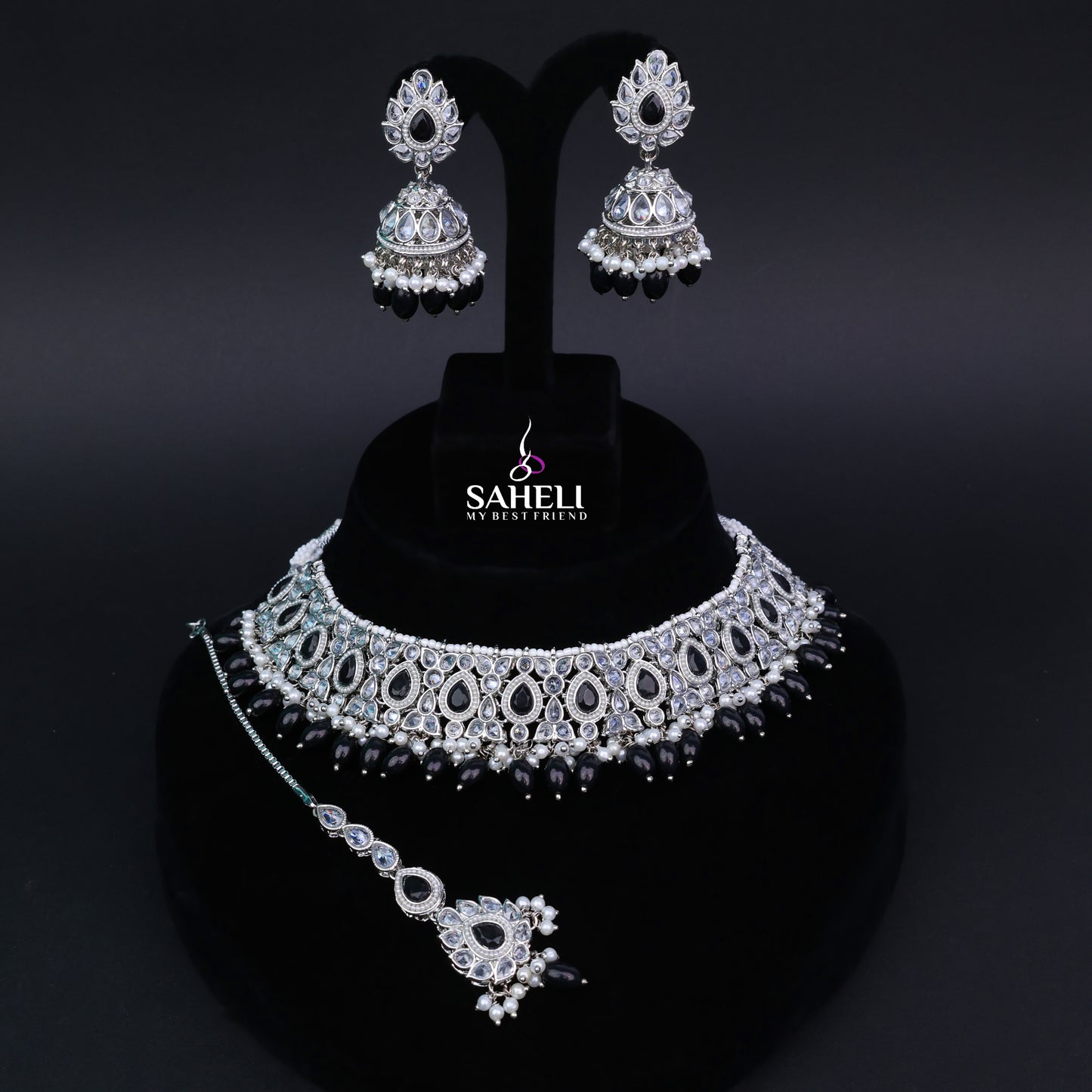 Jewelry set with necklace, earrings, and ring on a black stand with 'Saheli' branding.