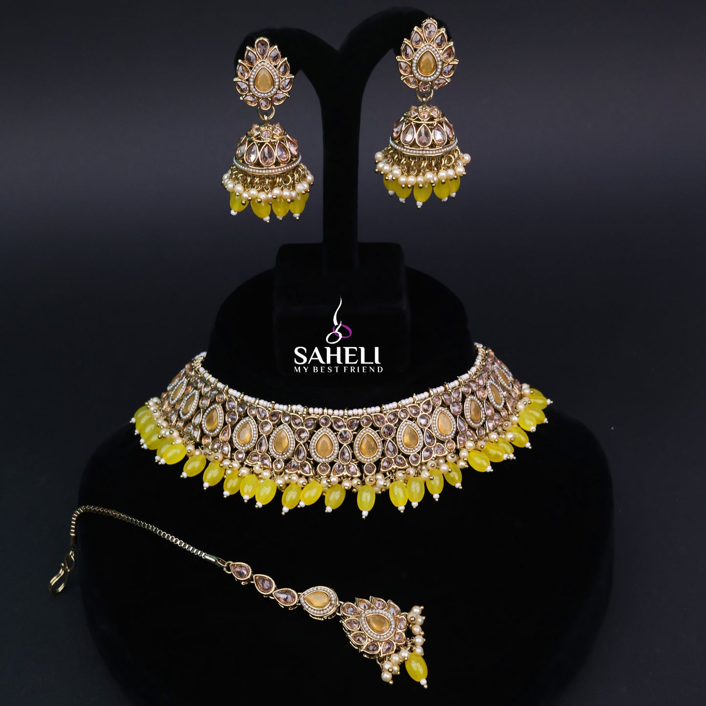 Jewelry set with necklace, earrings, and bracelet on a black stand with 'SAHELI' branding.