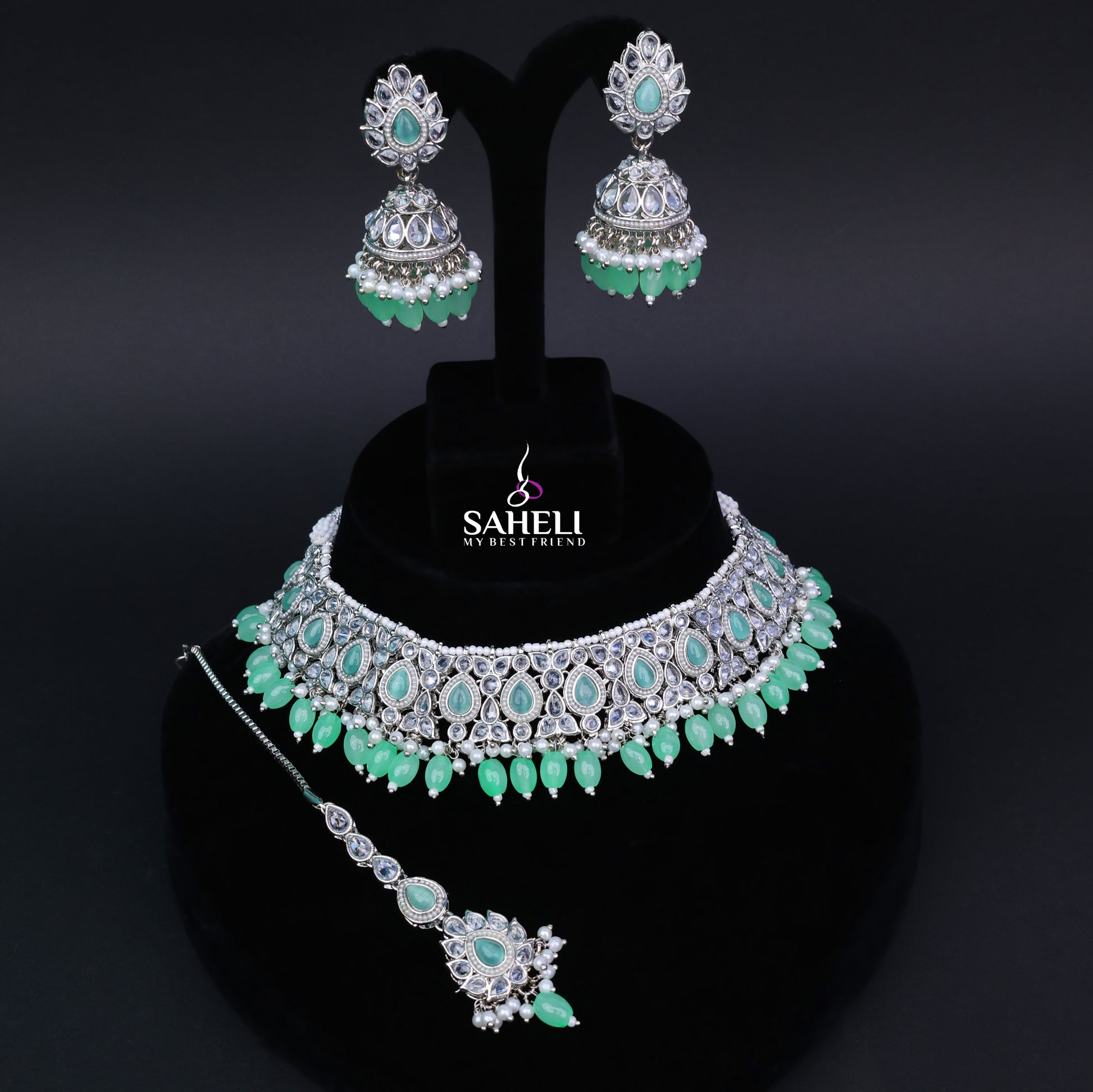 Jewelry set with necklace, earrings, and hairpin on a black stand with 'Saheli' branding.