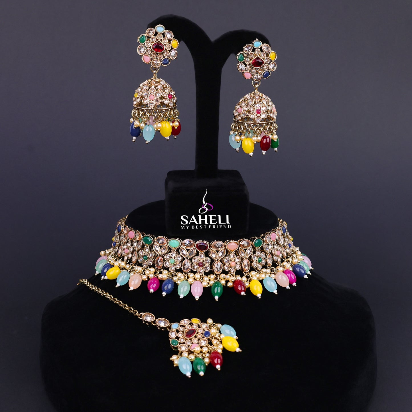 Jewelry set with colorful gemstones on a black stand with 'SAHELI' branding.