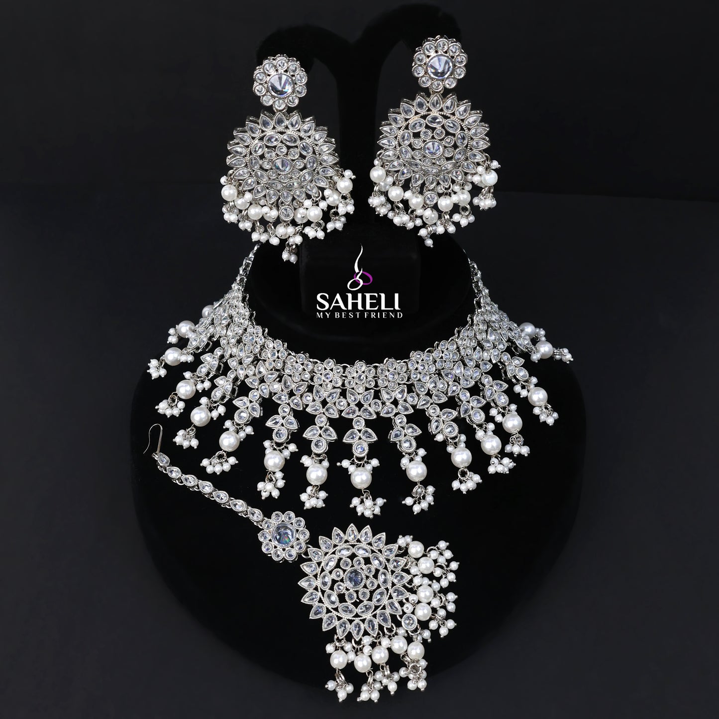Silver jewelry set with necklace, earrings, and ring on a black background with 'Saheli' branding.