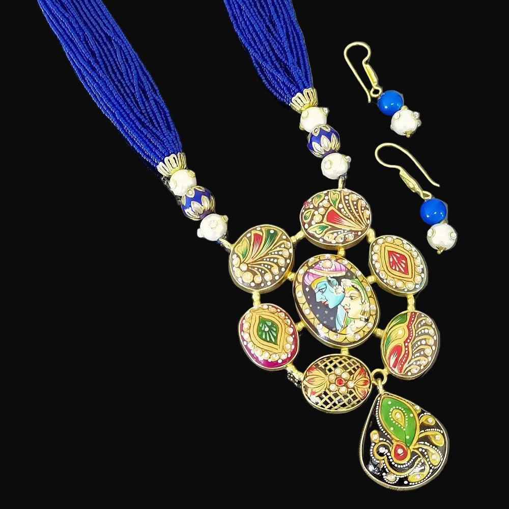 A traditional Indian jewelry set featuring a long necklace and matching earrings. The necklace has vibrant royal blue thread tassels, gold-plated metal, and colorful hand-painted clay ornaments (kumkum) in pink, green, and red.