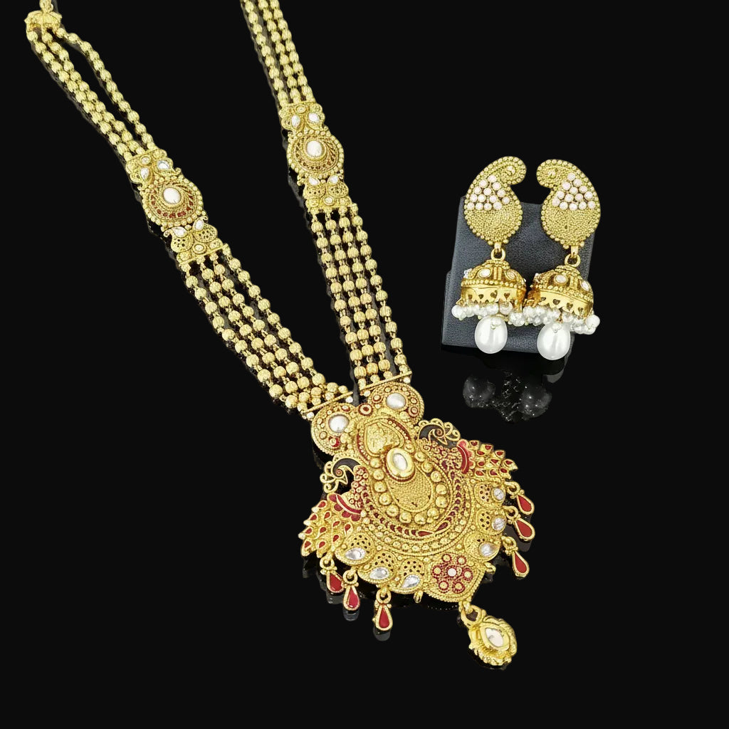 Gold-toned traditional Indian jewelry set featuring a double-strand beaded necklace with a large ornate pendant, matching drop earrings, and pearl-like accents, displayed on a dark reflective surface. The brand name 'SAHELI' is visible in the top right corner.