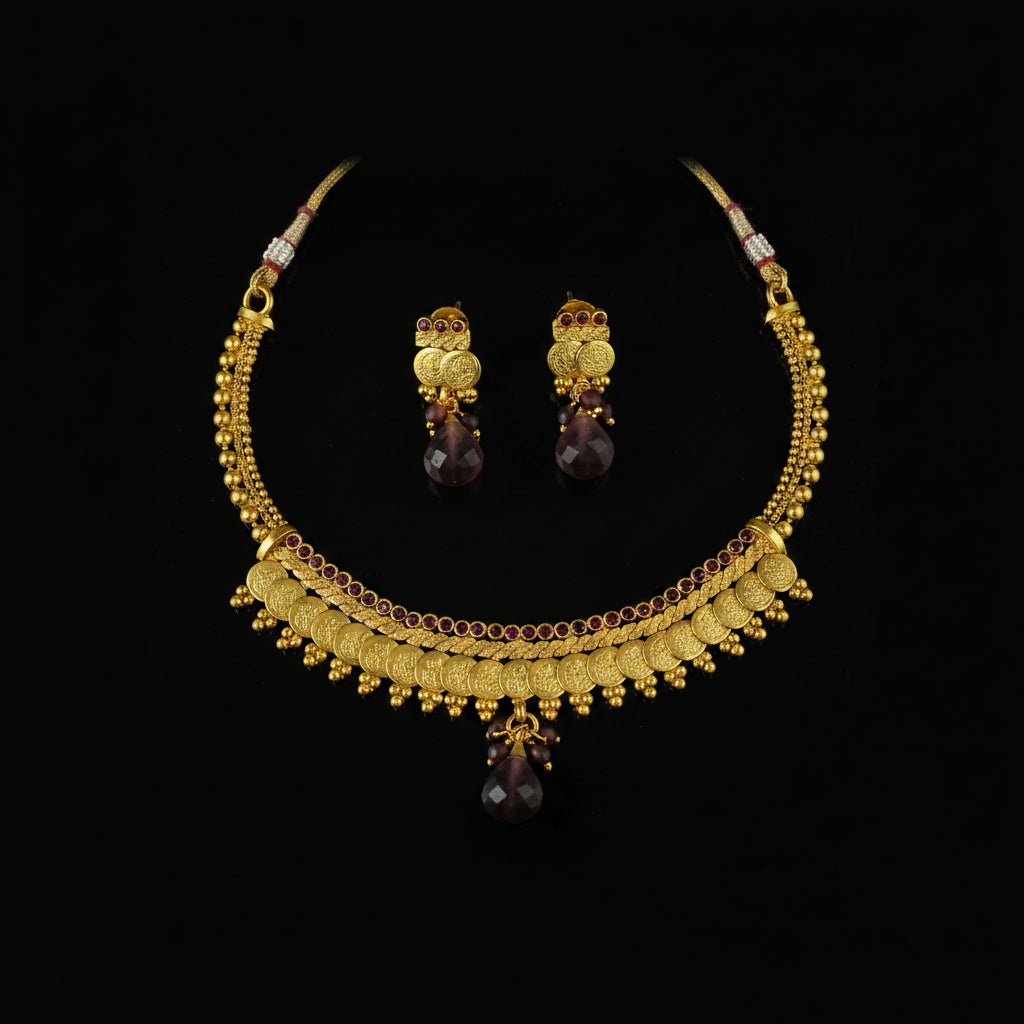 Gold-toned traditional necklace and matching earrings with dark purple teardrop stones, displayed on a dark reflective surface. The SAHELI MY BEST FRIEND logo is visible in the top left corner.