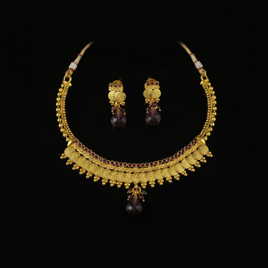Gold-toned traditional necklace and matching earrings with dark purple teardrop stones, displayed on a dark reflective surface. The SAHELI MY BEST FRIEND logo is visible in the top left corner.
