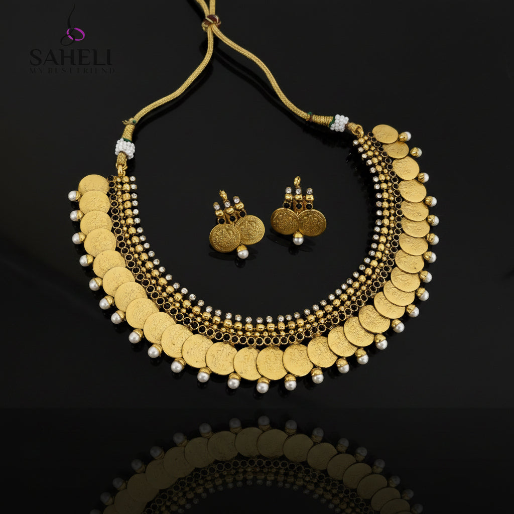 Gold coin necklace and matching gold coin earrings with white pearl accents, displayed on a dark gray reflective surface. The Saheli My Best Friend logo is visible in the top left corner.
