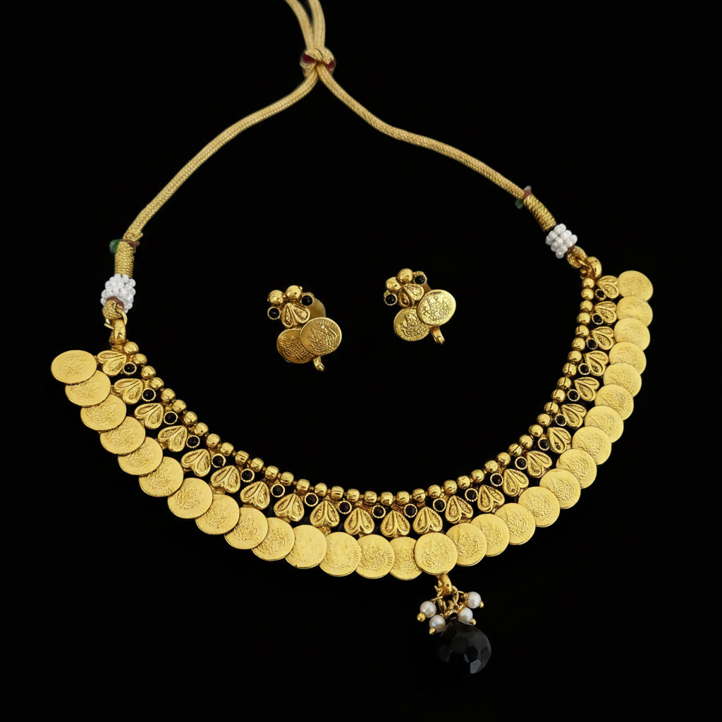 Gold coin necklace and matching stud earrings displayed on a dark reflective surface. The necklace features multiple rows of round gold coins, small bead details, and a dangling black faceted stone.