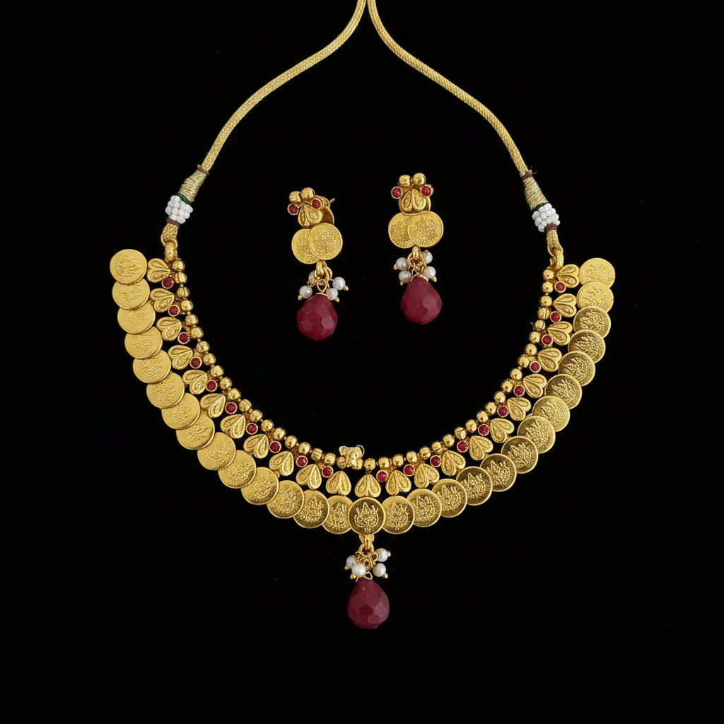 Gold coin-style necklace and matching earrings with red bead accents, displayed on a dark reflective surface. The necklace has a fan-shaped border, beaded details, and a dangling teardrop charm.
