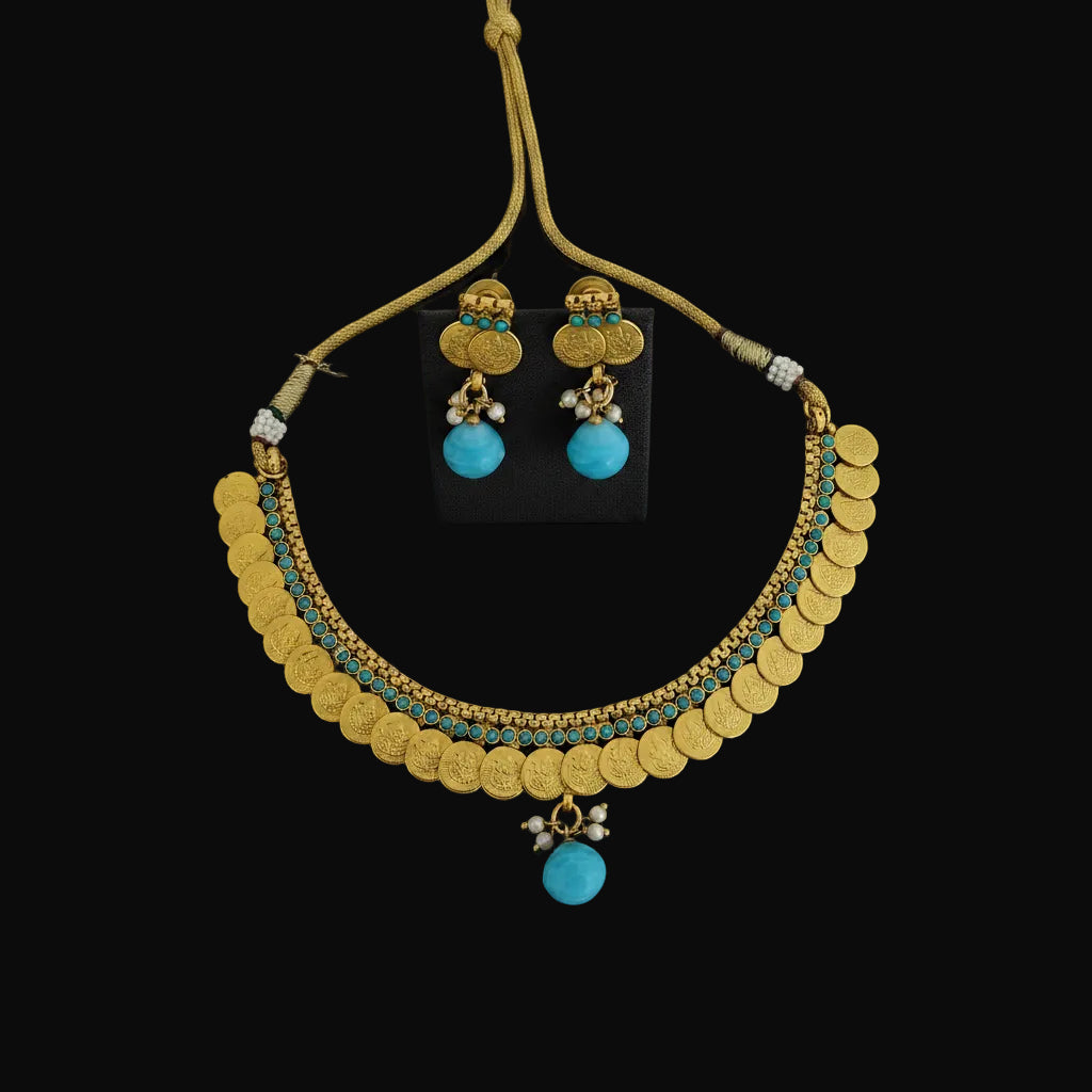 Gold coin-style necklace and matching earrings with turquoise blue bead drops and small white pearl accents, displayed on a dark reflective surface with a black jewelry stand. The brand name SAHELI MY BEST FRIEND appears in the top left.