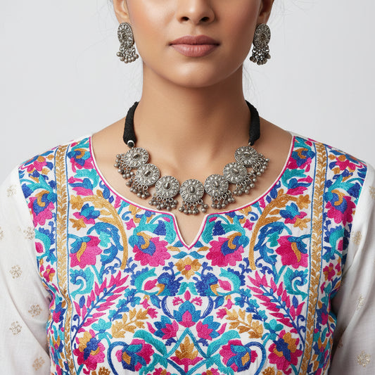 Silver necklace and earrings set with 'Saheli' branding on a gray background