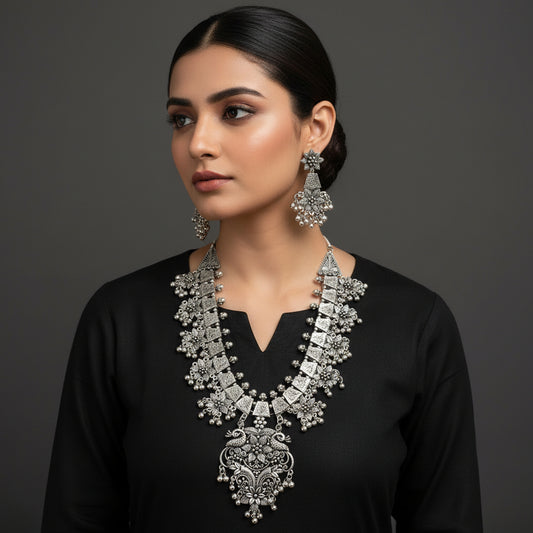 Silver necklace and earrings set with 'Saheli' branding on a gray background
