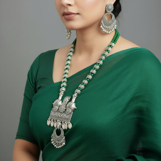 Silver necklace with green accents and matching earrings on a gray background, branded 'Saheli'.