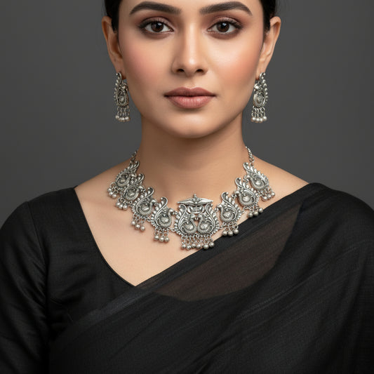 Silver jewelry set with necklace and earrings on a gray background, featuring the brand 'Saheli'.
