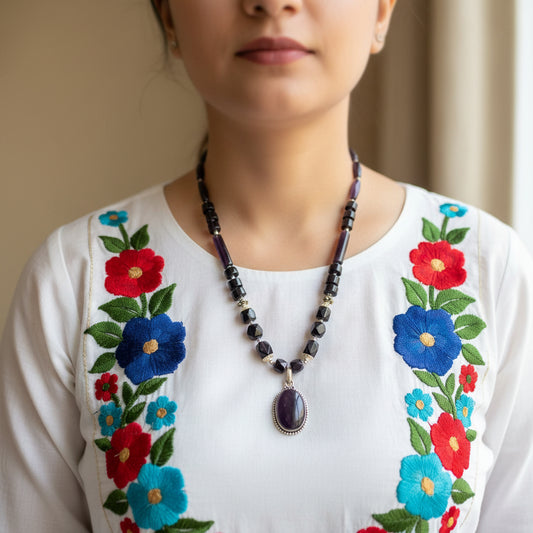 Necklace with black beads and a purple pendant on a reflective surface