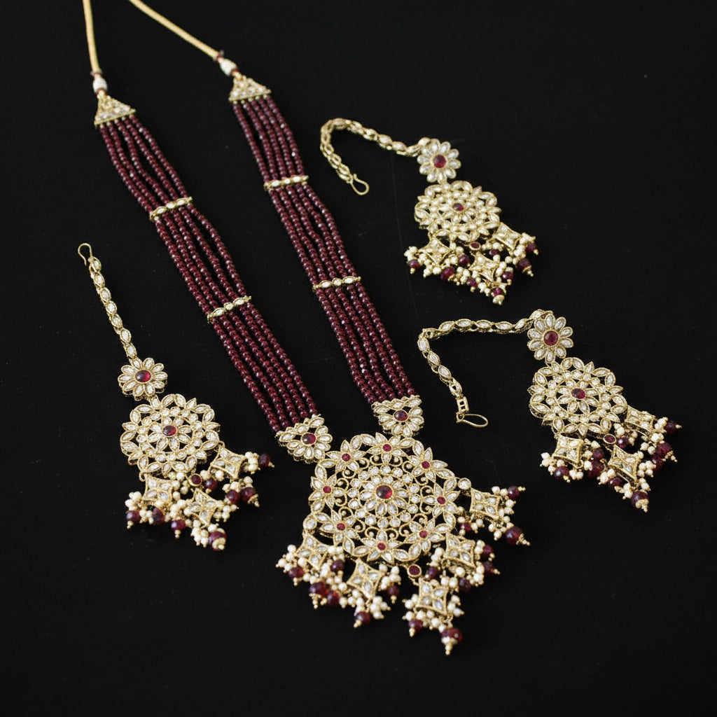 Jewelry set with maroon beads and gold accents on a gray background, featuring the brand 'Saheli'.