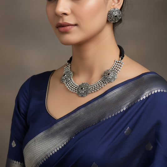 Silver necklace and earrings set with 'Saheli' branding on a gray background