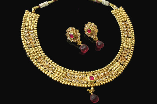 Gold necklace and earrings with red stones on a dark background, branded 'Saheli'.