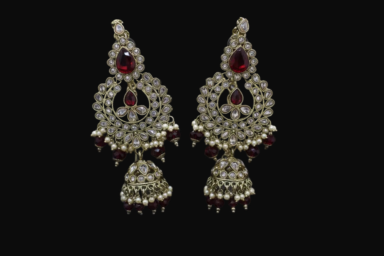 Ornate gold and red earrings on a stand with 'Saheli' branding.