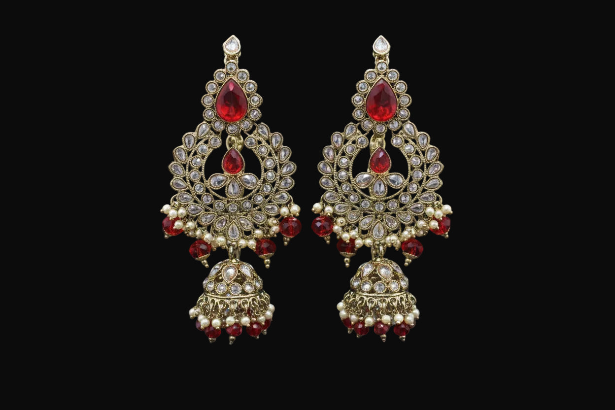 Ornate gold earrings with red gemstones on a stand against a dark background