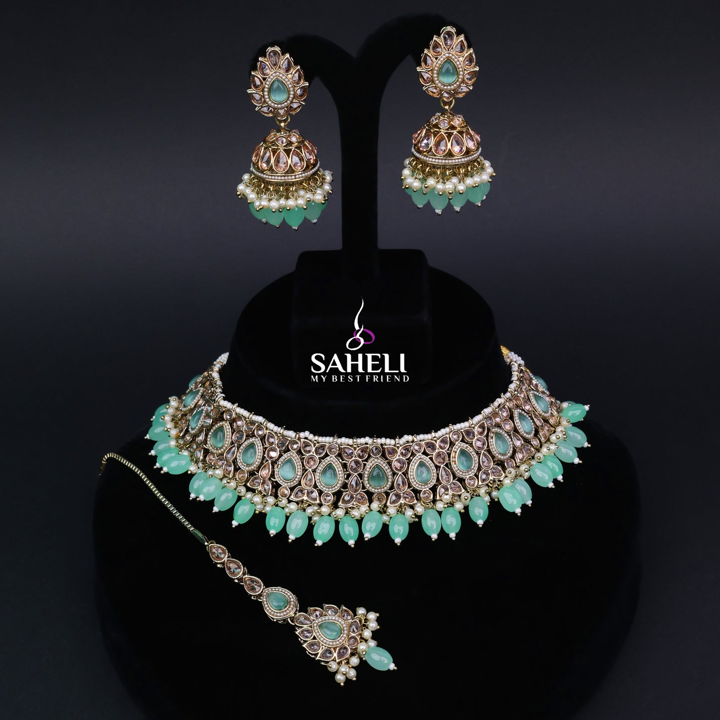 Jewelry set with necklace, earrings, and headband on a black stand with 'Saheli' branding.