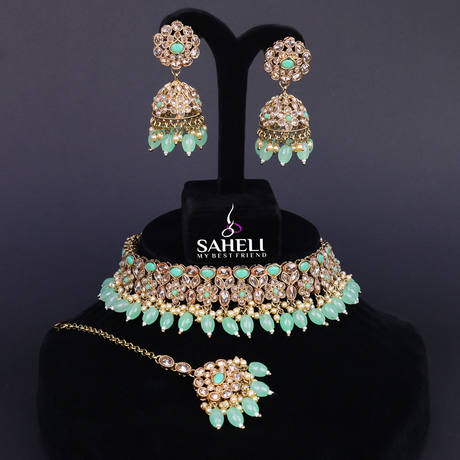 Jewelry set with necklace, earrings, and hairpin on a black stand with 'Saheli' branding.