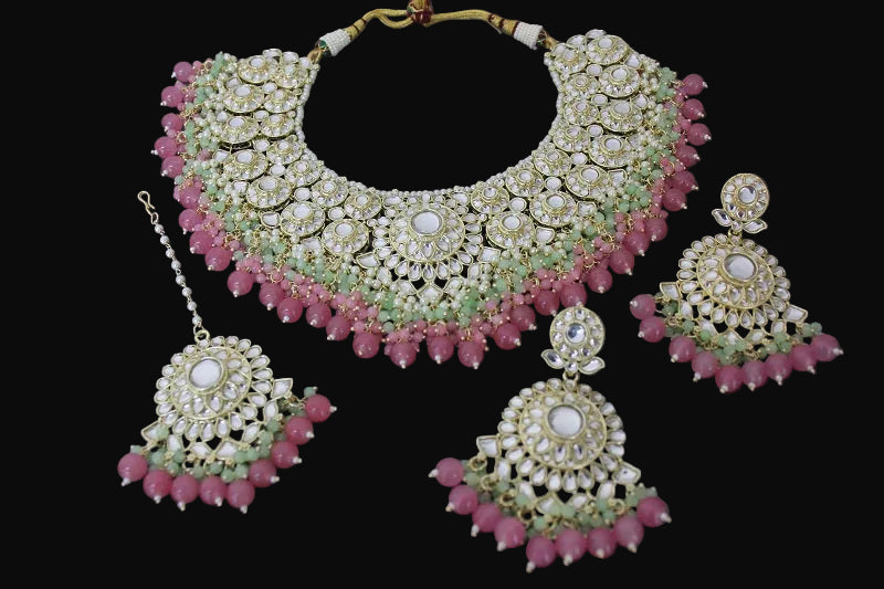 Ornate necklace and earrings set with pink and green stones on a dark background