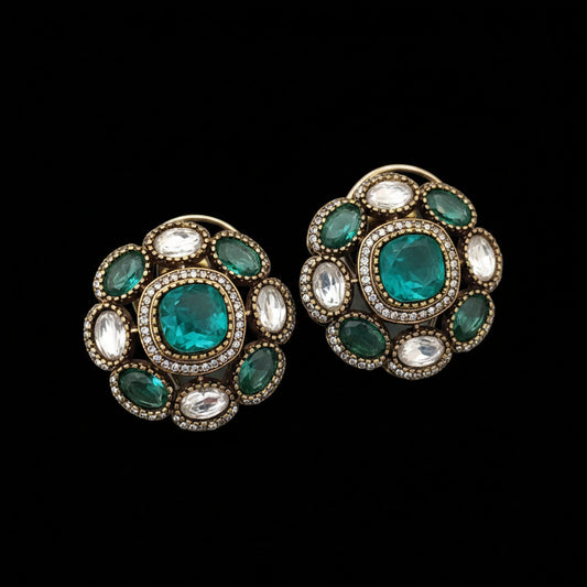 Pair of ornate earrings with green gemstones and 'SJNX-CODE-R-135' text on a light gray background.